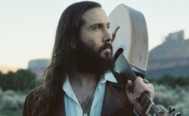 bearded man standing outside with guitar over shoulder