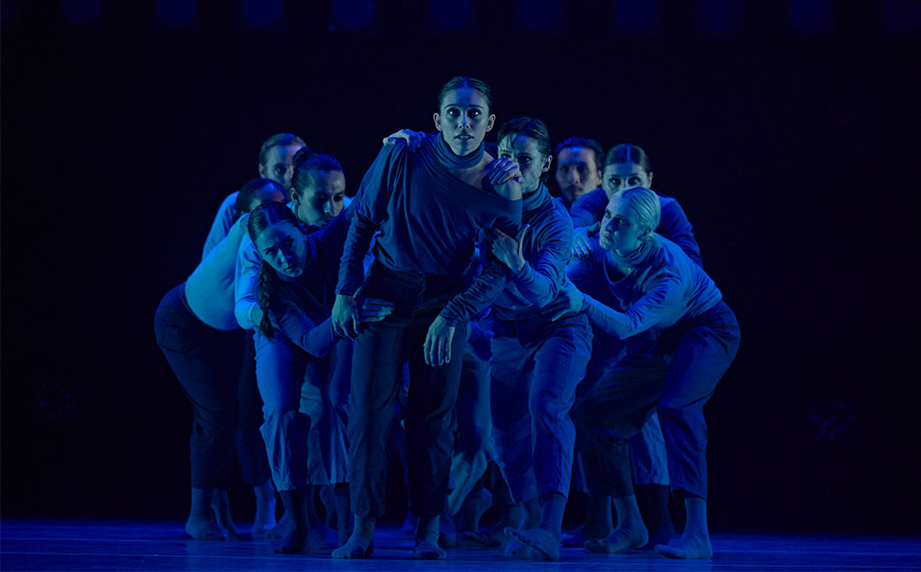 dancers huddled on stage under a blue light