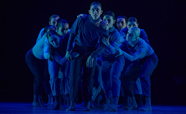 dancers on stage huddled under blue light