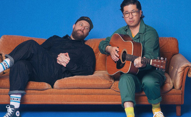 two men on a couch, one holding a guitar