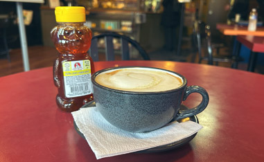 cup of coffee on a table next to a container of honey