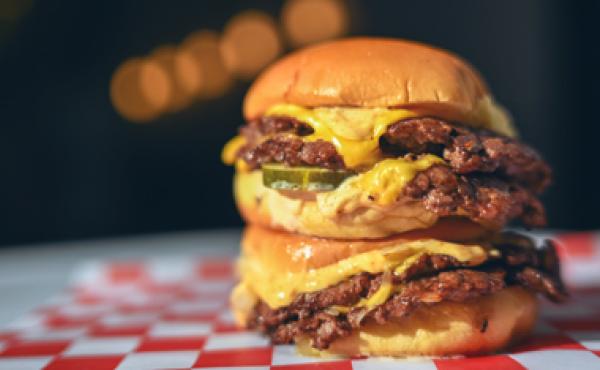 two smash burgers stacked on top of one another sitting on checkered paper on a table