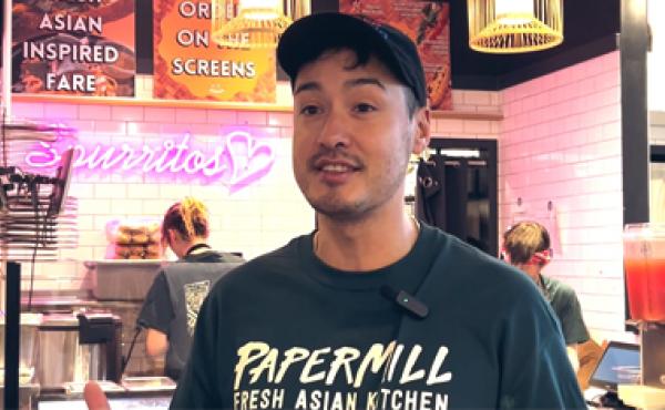 asian man in black papermill t-shirt standing in front of papermill food stall