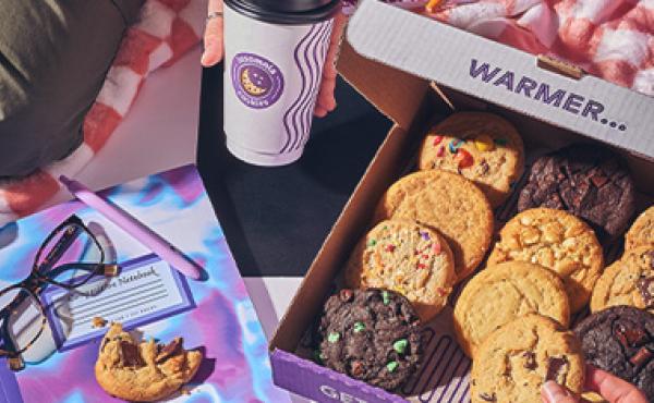 box of cookies on a blanket and a hand holding a coffee in an insomnia cup