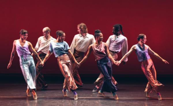 male and female dancers holding hands during a performance in front of a red background