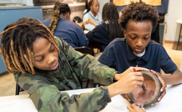 two african american boys painting a pot in a classroom