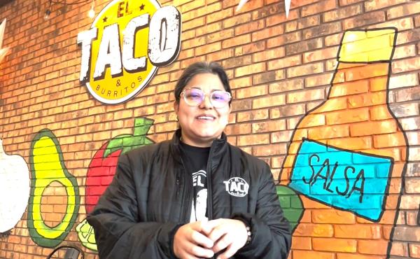woman wearing glasses in black jacket standing in front of el taco store signage